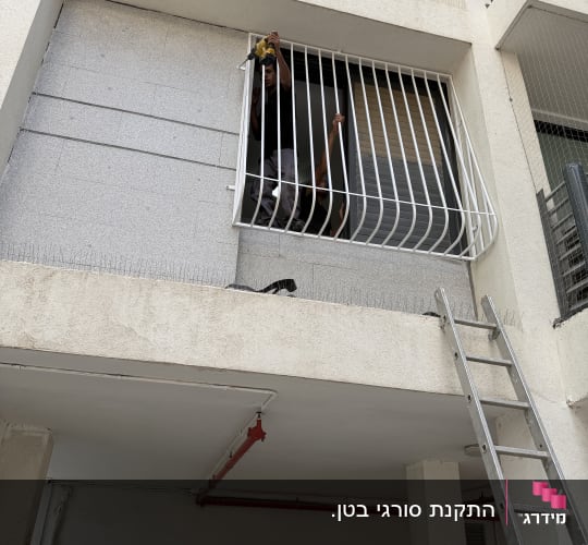 אדם מתקין סורגים על חלון בניין עם סולם